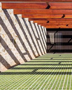 an outdoor area with green grass and brick walls, covered in wooden slatted roofing