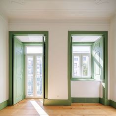 an empty room with two green doors and windows on the wall, along with hard wood flooring