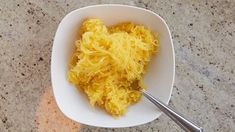 a white bowl filled with shredded cheese on top of a counter next to a spoon