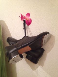 a pair of black shoes hanging on a wall with a pink flower in the middle