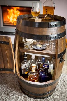 a wooden barrel filled with bottles and glasses on top of a carpeted floor next to an open fire place