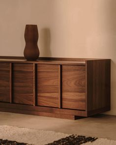 a vase sitting on top of a wooden cabinet next to a rug in a room