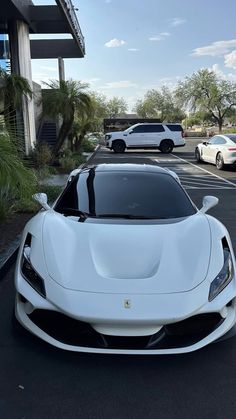 a white sports car is parked in front of a building with other cars behind it