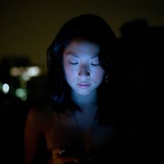 a woman is looking at her cell phone in the dark with city lights behind her