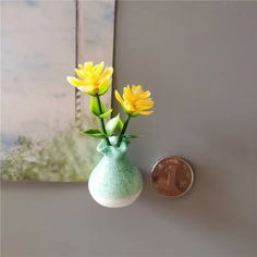 two yellow flowers in a green vase next to a one euro coin on the wall