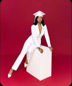 a woman in a white suit and cap sitting on top of a cube