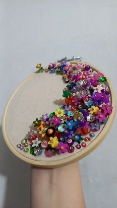 a hand is holding a small embroidery project with colorful beads and buttons on it's side