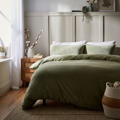 a bed with green linens and pillows in a bedroom next to a white wall