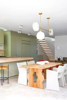 an open kitchen and living room with stairs leading up to the second floor, along with a dining table surrounded by white chairs