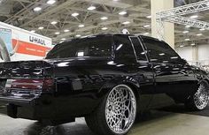 a black car parked in a garage next to another vehicle with chrome wheels and rims