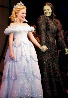 two people dressed in costumes standing next to each other on stage with one holding the hand of another person's hand