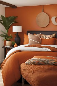 a bed with orange sheets and pillows in a bedroom next to a plant on the wall