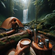 a man sitting in front of a waterfall next to a tent with a cup of coffee