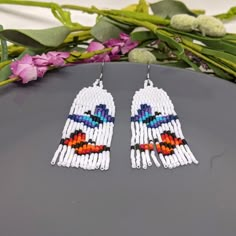 the beaded earrings are designed with colorful beads and fringes, which have been placed on top of a gray surface