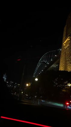 cars driving down the road at night in front of a bridge