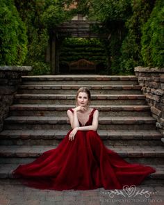 a woman in a red dress is sitting on some steps and looking at the camera