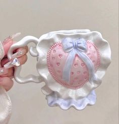 a hand holding a pink and white ceramic teapot with a bow on it's handle