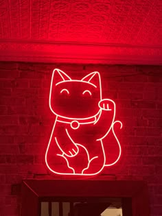 a red neon sign with a cat on it's side in front of a brick wall