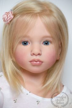 a doll with blonde hair and blue eyes wearing a pink flower in her hair is looking at the camera