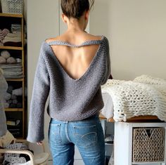 a woman standing in front of a mirror wearing jeans and a sweater with open back