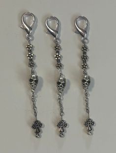 three pairs of dangling earrings with skulls and clovers on them, all in silver