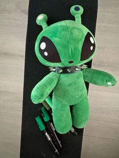 a green alien stuffed animal sitting on top of a skateboard with pens and markers