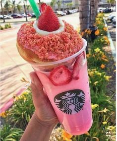 a person holding up a pink drink with strawberries on top and topped with whipped cream