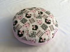 a pink and black flowered round cushion sitting on top of a white sheet