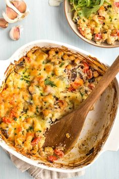 a casserole dish with cheese and vegetables in it, next to a wooden spoon