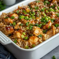 a white casserole dish with chicken, rice and green onions in it on a table