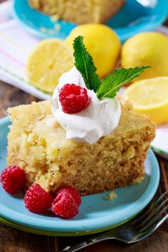 a piece of cake on a blue plate with raspberries and lemons next to it