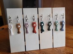 six different keychains are hanging from hooks on a wooden stand, each with tassels attached to them