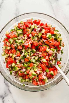 a glass bowl filled with cucumber, tomato and onion salad on top of a marble counter