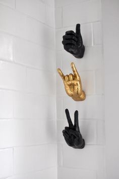 three black and gold hand sculptures hanging on the wall in a white tiled shower stall