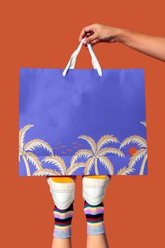 two hands holding up a blue shopping bag with palm trees on it and white handles