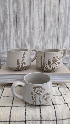 two mugs sitting on top of a table next to an open book with flowers painted on them