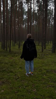 a person standing in the middle of a forest looking at some tall trees and grass