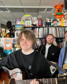 two men are playing guitars in front of bookshelves with stuffed animals on the shelves behind them