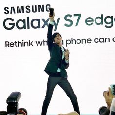 a man in a suit is holding up his cell phone while standing on stage with people around him