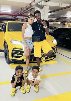 three kids posing in front of a yellow car with their hands on the hood and two men standing next to them