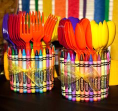 colorful plastic utensils are lined up in small cups on a table with ribbons