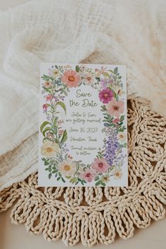 save the date card with flowers on it sitting on a doily next to a white blanket