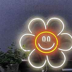 a neon sign with a smiley face on it's side next to a potted plant