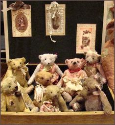 a group of teddy bears sitting next to each other in a wooden box with pictures on the wall behind them