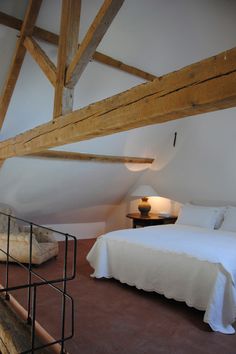 a bed sitting under a wooden beam in a bedroom next to a table with a lamp on it