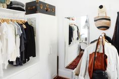 a closet with clothes and handbags hanging on the wall, next to a mirror