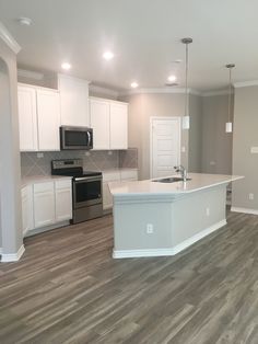 an empty kitchen and living room in a new home with wood flooring, stainless steel appliances and white cabinets