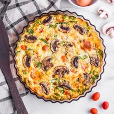 an egg and vegetable quiche on a table with tomatoes, mushrooms, and eggs