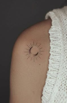 a woman's shoulder with a small sun and moon tattoo on it