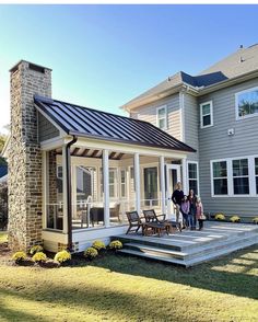 two people standing on the front porch of a house with an attached patio and deck